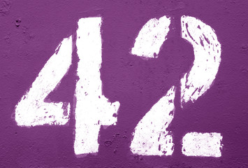 Number 42 in stencil on rusty metal wall in purple tone.