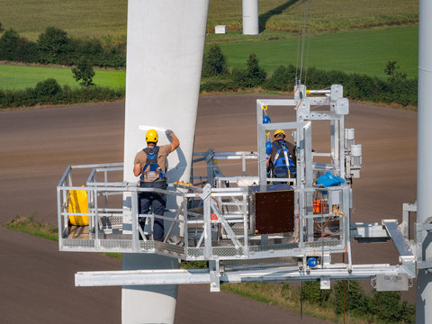 Workers on a hanging platform repair a damaged rotor blade on a wind turbine