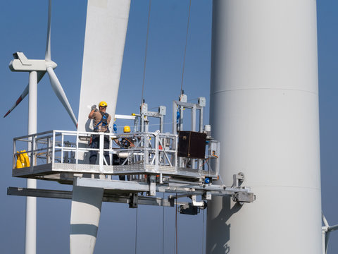 Workers on a hanging platform repair a damaged rotor blade on a wind turbine