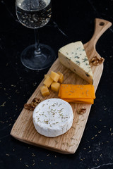 Tasting cheese dish on a wooden plate. Cheese assorted - blue cheese, camembert, cheddar and parmesan. Food for wine and romantic, cheese delicatessen on a black marble table. Top view with copy space