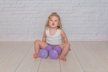 girl, the child is engaged in fitness with dumbbells, against a white brick wall