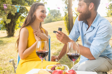 Man showing to beautiful girlfriend an engagement ring during romantic picnic