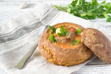 Traditional Hungarian Goulash soup with parsley and green onions in a bread on a white and brown rustic background with copy space