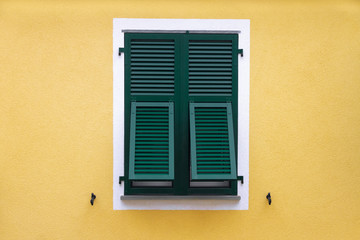 green wooden window with shutters in a white frame on the yellow wall
