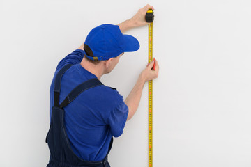 The builder measures the distance on a white wall with a tape measure