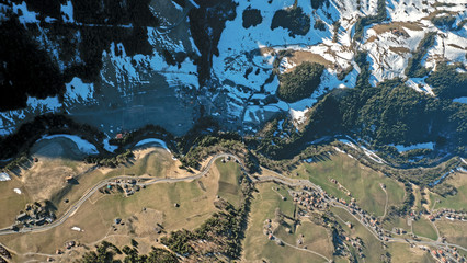 Stunning top down aerial views of mountain river valley high in the Swiss alps. The river winds its way through the valley floor surrounded by snow patches and fields.