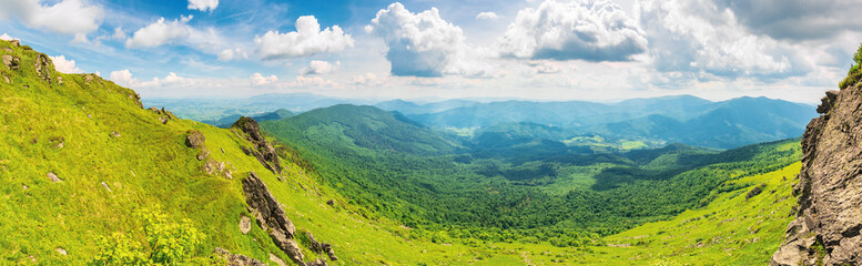 panorama of a valley in summer. beautiful landscape with rocks on grassy hills. distant ridge beneath a blue sky with fluffy clouds. wonderful sunny weather. view from the mountainside