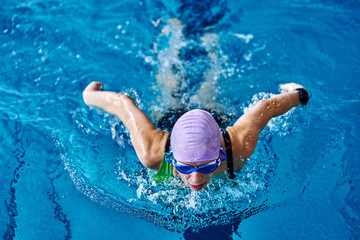 Female athlete swims with a butterfly style. Splashes of water scatter in different directions.