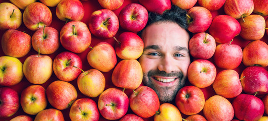 Mann mit roten Äpfeln, Konzept für die Lebensmittelindustrie. Gesicht des verziehenden Mannes im Apfelbereich