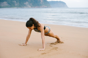 Fit young woman in bikini doing push ups strength exersice at the beach. Outdoor fitness and healthy lifestyle.