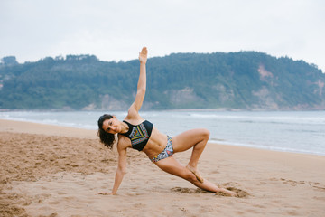 Fototapeta na wymiar Fit young woman in bikini doing balance yoga exersice at the beach. Outdoor fitness and healthy lifestyle.