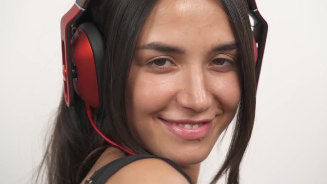 A close-up of an attractive girl wearing headphones, listening to music and temptingly smiling