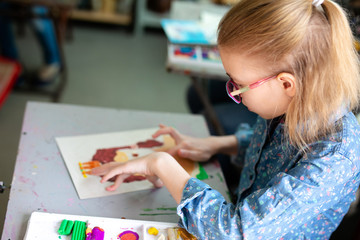 Portrait of adorable little girl smiling happily while enjoying art and craft lesson in art school working together with other kids