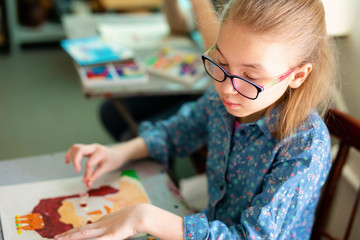 Portrait of adorable little girl smiling happily while enjoying art and craft lesson in art school working together with other kids