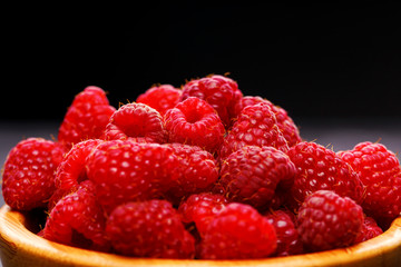 Photo of raspberries in wooden cup on black background