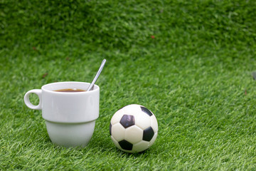 Football wiht cup of coffee on green grass