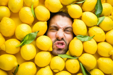Mann mit Zitronen, Konzept für die Lebensmittelindustrie. Gesicht des lachenden Mannes in der Zitronenoberfläche. - obrazy, fototapety, plakaty