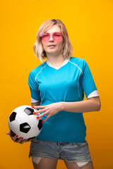 Photo of blonde in pink glasses with soccer ball on orange background