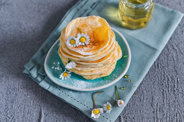 Many small pancakes with honey or syrup. Delicious traditional breakfast. Spring flowers as food styling in photography. Gray stone background and dessert is sweet. Free space for the test.