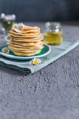 Many small pancakes with honey or syrup. Delicious traditional breakfast. Spring flowers as food styling in photography. Gray stone background and dessert is sweet. Free space for the test.