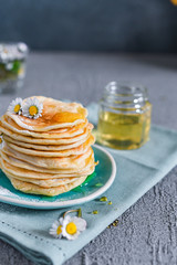 Many small pancakes with honey or syrup. Delicious traditional breakfast. Spring flowers as food styling in photography. Gray stone background and dessert is sweet. Free space for the test.
