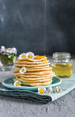 Many small pancakes with honey or syrup. Delicious traditional breakfast. Spring flowers as food styling in photography. Gray stone background and dessert is sweet. Free space for the test.