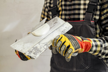 Young male builder and repairman in a yellow helmet plastering the wall with a spatula and plaster.