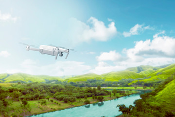 Fototapeta na wymiar White drone with camera flying over green hills with river and trees