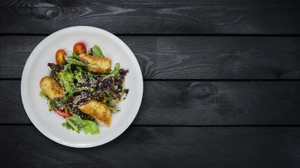 Salad with salmon in breadcrumbs with lettuce and sesame seeds. Rotates on black wooden background. Top view with the copy space for your text.