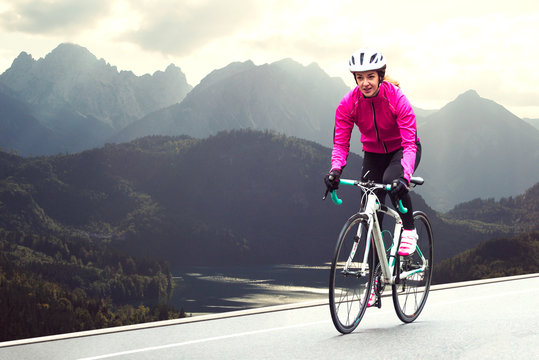 Young Woman in Bright Pink Jacket Riding Road Bicycle on Mountain Alpine Road. Healthy Lifestyle and Adventure Concept. - Powered by Adobe