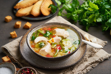 Homemade chicken soup with vegetables, crouton, broccoli on a dark brown background, side view
