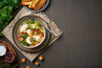 Obraz na płótnie Canvas Homemade chicken soup with vegetables, broccoli on a dark brown background, top view, copy space
