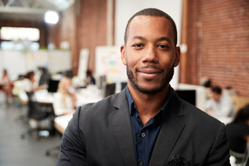 Portrait Of Businessman In Modern Open Plan Office With Business Team Working In Background
