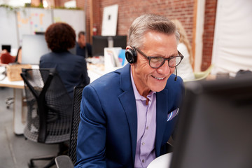 Mature Male Customer Services Agent Working At Desk In Call Center