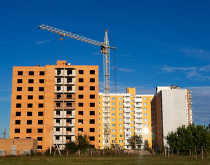 Fototapeta na wymiar Construction of new apartment building. Facade of unfinished brick multistory building with crane and new dwelling on the background