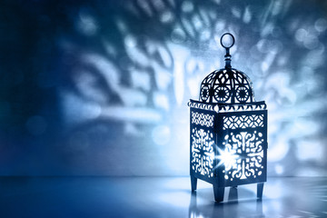 Fototapeta na wymiar Silhouette of Moroccan lantern with burning glowing candle. Decorative shadows. Festive greeting card, invitation for Muslim holy month Ramadan Kareem. Blue night background with bokeh lights.