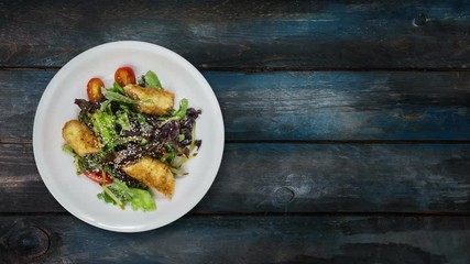 Salad with salmon in breadcrumbs with lettuce and sesame seeds. Rotates on wooden background. Top view with the copy space for your text.