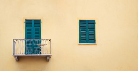 Fototapeta na wymiar metallic lilac balcony with green sash door and wooden window with shutters in orange frame on yellow wall