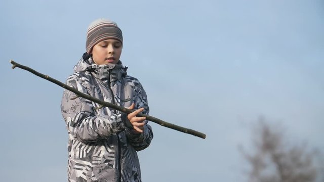 Small boy in a spring jacket turning a long stick around in a field in spring in slo-mo  