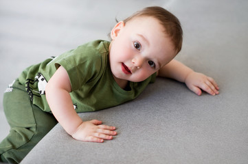 Fototapeta premium One-year-old boy tries to climb on a gray sofa.