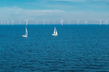 Alternative energy - row of offshore wind turbines and yachts at sea, green energy windmill...