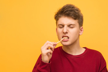 Young man bites fries with closed eyes on a yellow background. Guy eats eating fried potatoes, isolated. Copyspace