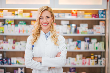 Portrait of a smiling pharmacist with arms crossed at modern pharmacy. - obrazy, fototapety, plakaty