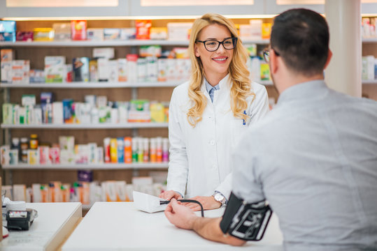 Blonde Pharmacist Measuring Blood Pressure To Young Male Patient.