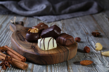 Chocolates in different shapes and colors over rustic wooden board. Atmospheric food photo