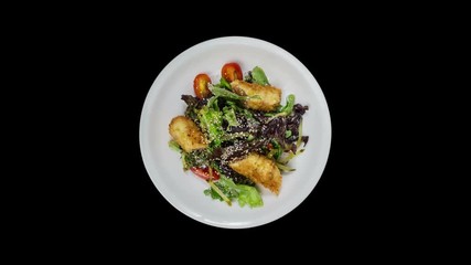 Salad with salmon in breadcrumbs with lettuce and sesame seeds. Isolated on the black background.