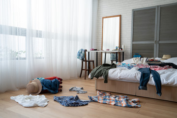 straw hat and colorful clothes in luggage on wooden floor. empty nobody in messy white bed in...