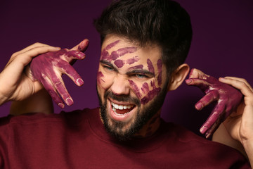 Portrait of handsome man with paint on his face and female hands against color background