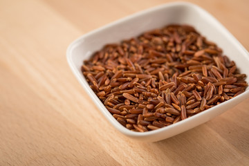 Rotschaliger roher Roter Jasmin Reis in Porzellan Schale auf Holz Hintergrund und ist eine Spezialität aus Kambodscha Asien