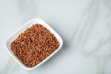 Rotschaliger roher Roter Jasmin Reis in Porzellan Schale auf Marmor Hintergrund und ist eine Spezialität aus Kambodscha Asien